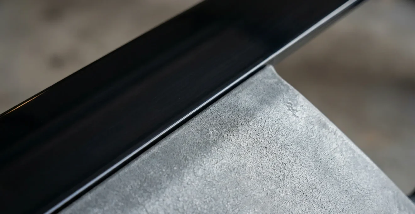 Gros plan sur un pare-chocs automobile montrant une partie traitée noire et une partie ternie et grise par le soleil