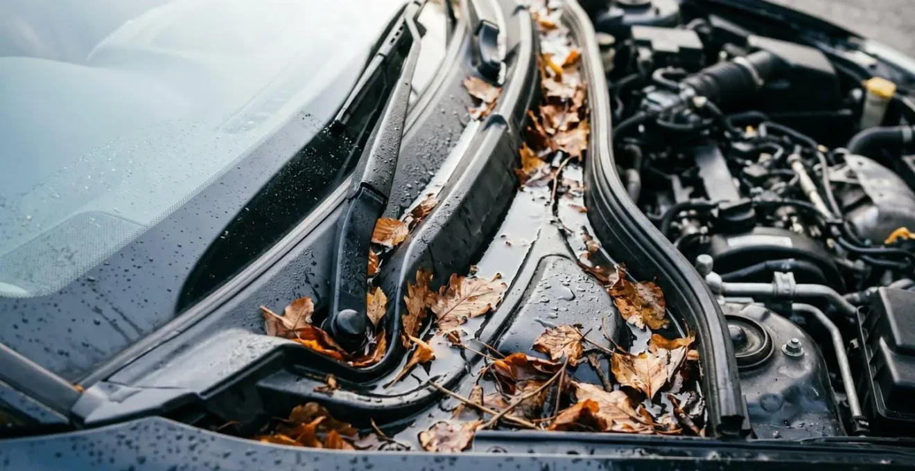 Vue détaillée des drains d'évacuation d'eau sous le capot d'une voiture avec feuilles accumulées